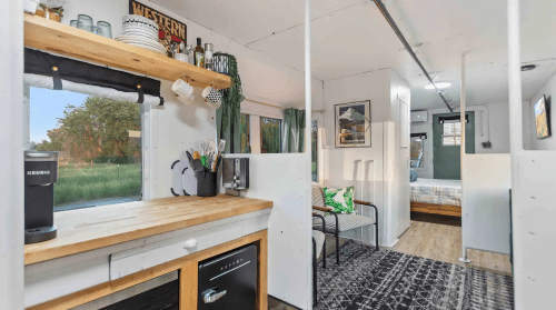 Cozy interior of a tiny home with a kitchen, seating area, and a view of greenery outside.