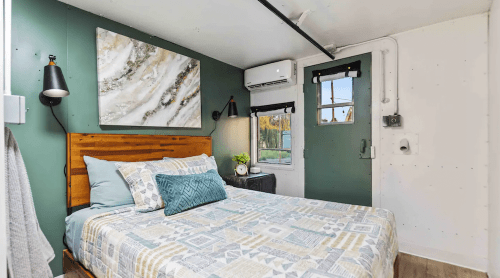 Cozy bedroom with a wooden bed, patterned bedding, green walls, and a modern art piece above the headboard.