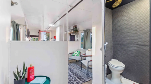 Interior of a compact living space featuring a shower, toilet, and a cozy seating area with a rug.