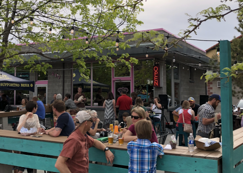 A lively outdoor scene at a restaurant with people dining, socializing, and enjoying the atmosphere under string lights.