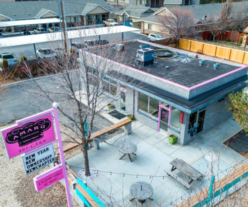 Aerial view of a café with a pink sign, outdoor seating, and nearby houses in a residential area.