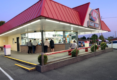 A Dairy Queen Grill & Chill restaurant at dusk, with customers ordering at the window and a few seated outside.