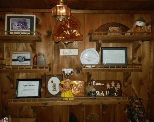 A wooden shelf displays various framed pictures, awards, and decorative items, including a bear figurine and gingerbread decor.