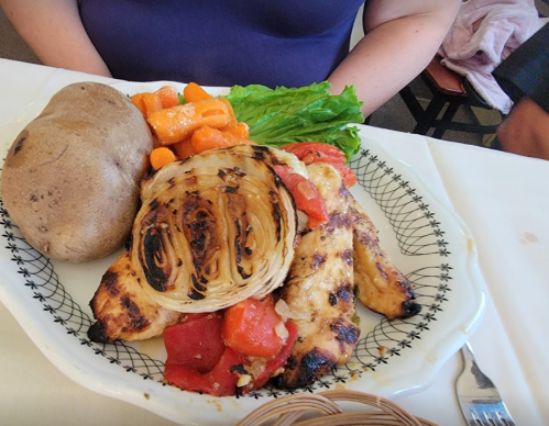 A plate with grilled chicken, roasted cabbage, baked potato, and carrots, served on a decorative dish.