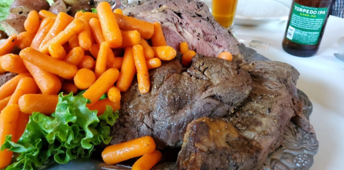 A platter of roasted beef surrounded by bright orange carrots and fresh lettuce, with a drink in the background.