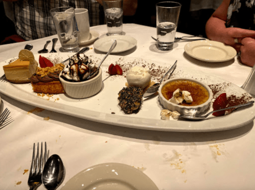 A dessert platter featuring various sweets, including cheesecake, ice cream, and crème brûlée, garnished with strawberries.