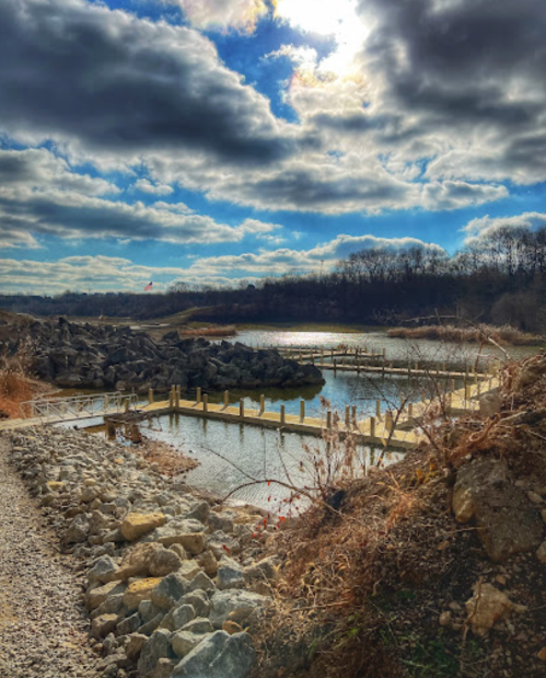 A serene landscape featuring a calm waterway, rocky shore, and cloudy sky, with a wooden dock in the distance.