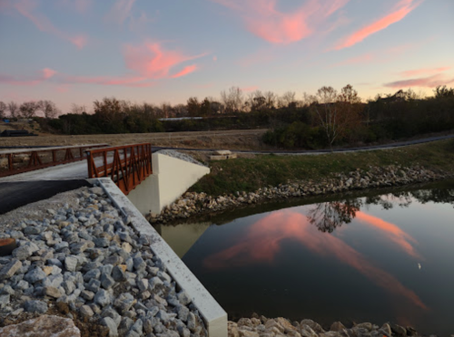 A serene landscape featuring a bridge over a calm waterway, with colorful clouds reflecting at sunset.