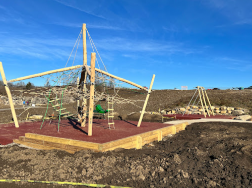 A playground under construction featuring climbing structures and swings, set against a clear blue sky.