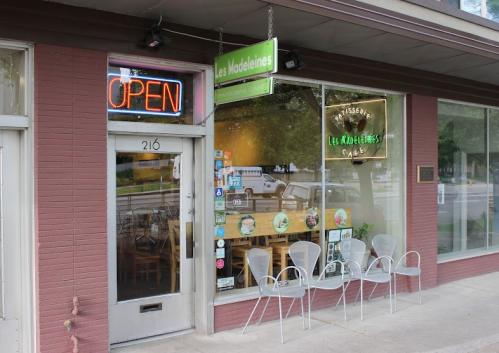 Exterior of Les Madeleines café with an "Open" sign, featuring outdoor seating and a welcoming storefront.
