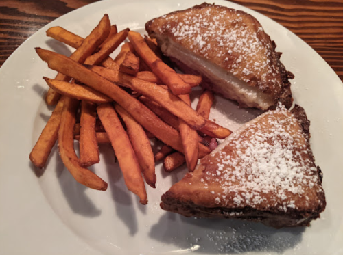 A plate with two pieces of French toast dusted with powdered sugar, accompanied by a side of golden French fries.
