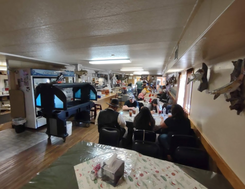 A busy indoor space with people seated at tables, engaged in activities, and various items displayed on the walls.