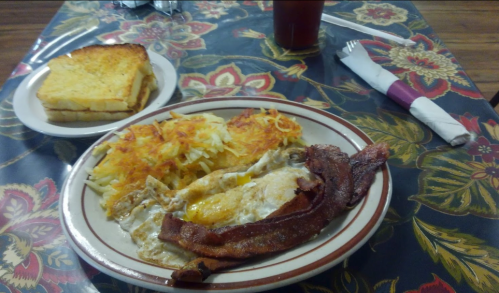 A plate of eggs, hash browns, and bacon, with a side of buttered toast on a floral tablecloth.