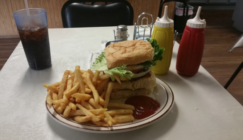 A plate with a large sandwich topped with lettuce and tomato, served with a side of fries and condiments.