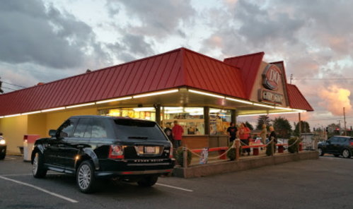 A fast-food restaurant with a red roof, featuring a black SUV parked outside during sunset.