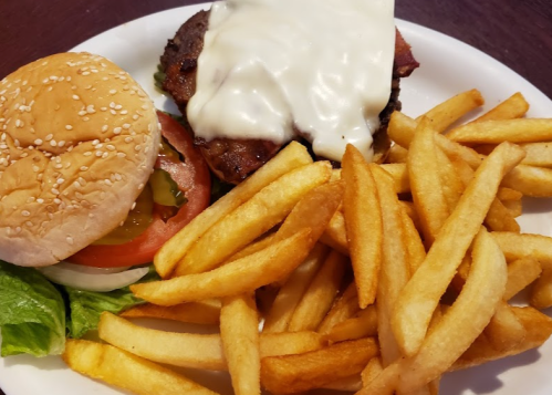 A plate with a cheeseburger topped with melted cheese, lettuce, and tomato, alongside a serving of golden French fries.