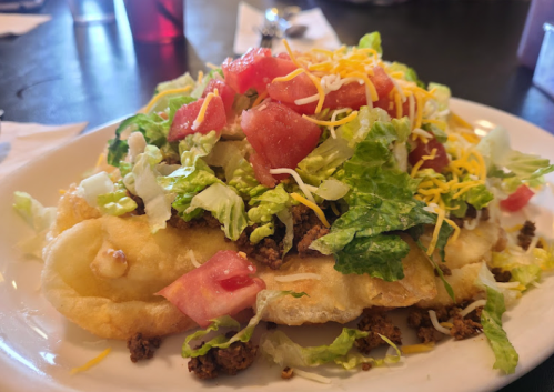 A loaded taco salad on a plate, featuring ground meat, lettuce, tomatoes, cheese, and a crispy shell.