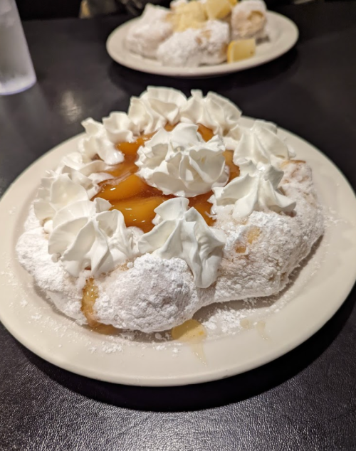 A dessert plate featuring a fluffy pastry topped with whipped cream and fruit filling, dusted with powdered sugar.