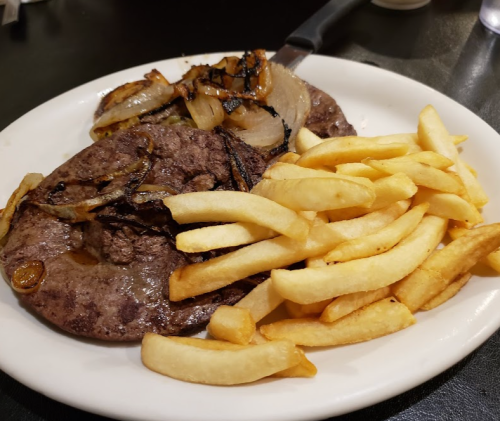 A plate of grilled beef with sautéed onions and a side of golden French fries.