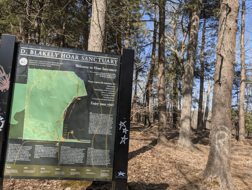 Sign for D. Blakely Hoar Sanctuary with a map and welcome message, surrounded by trees and natural landscape.