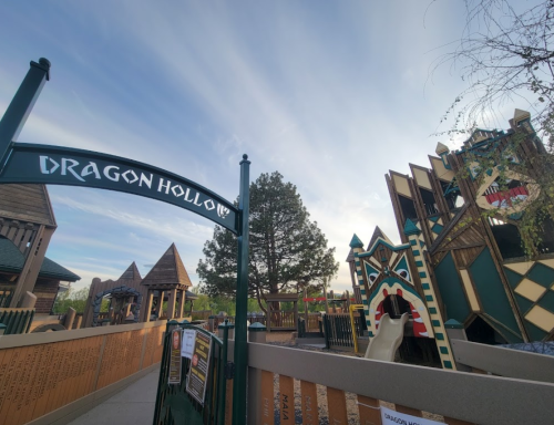 Entrance to Dragon Hollow playground, featuring whimsical structures and a clear blue sky in the background.