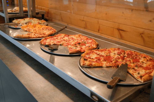 A selection of pizzas on metal trays, including pepperoni, veggie, and cheese, displayed on a buffet table.