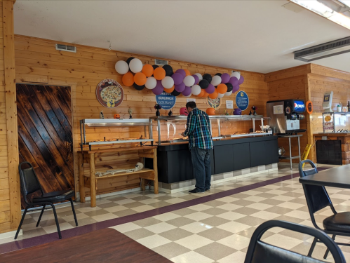A person serves food at a buffet in a wooden-paneled restaurant decorated with balloons.