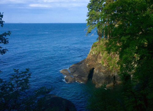 A serene coastal view featuring rocky cliffs, lush greenery, and calm blue waters under a clear sky.