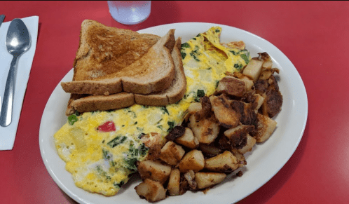 A plate of breakfast featuring an omelet with vegetables, toast, and crispy potatoes on a red table.