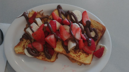 A plate of French toast topped with sliced bananas, strawberries, and drizzled chocolate.