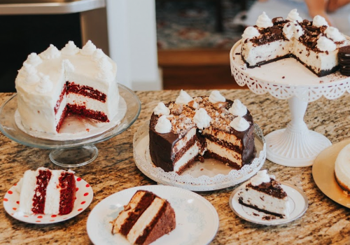 A variety of cakes displayed on a countertop, including red velvet, chocolate, and a layered white cake with toppings.