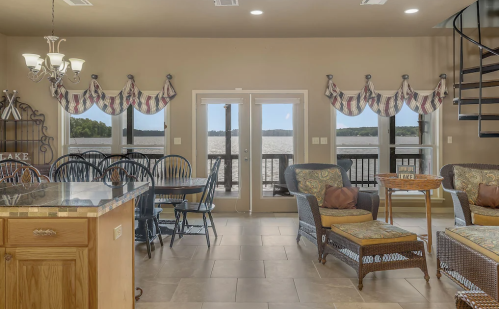Cozy lakefront living area with dining table, spiral staircase, and large windows showcasing scenic water views.