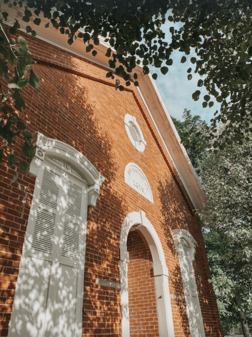 A brick building with white trim, partially shaded by leaves, under a clear blue sky.