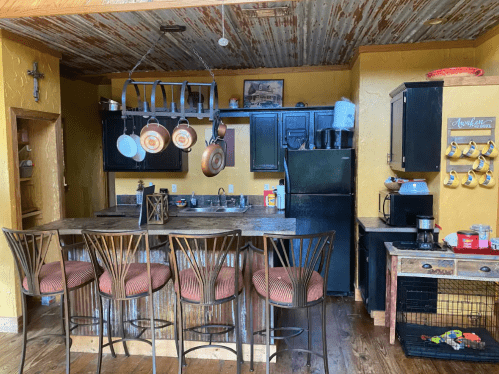 A rustic kitchen with a metal ceiling, dark cabinets, a bar with stools, and various kitchen appliances and decor.