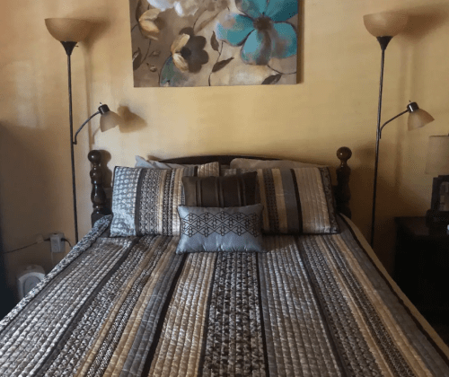 A cozy bedroom featuring a neatly made bed with patterned bedding and two lamps on either side.