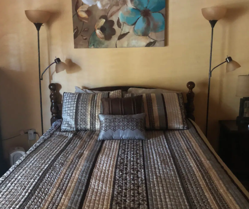 A cozy bedroom featuring a neatly made bed with patterned bedding and two lamps on either side.