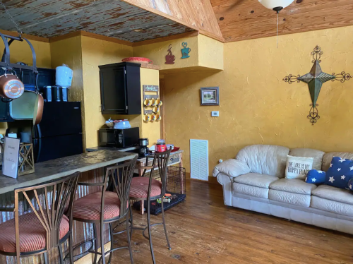 Cozy kitchen and living area with a bar, couch, and rustic decor in warm colors.