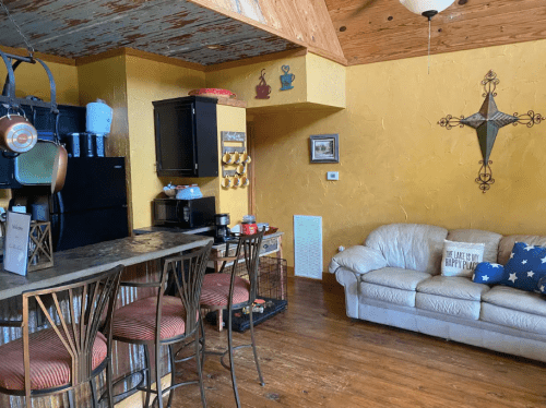 Cozy kitchen and living area with a bar, couch, and rustic decor in warm colors.