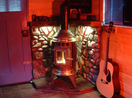 Cozy room featuring a stone fireplace with a wood stove and an acoustic guitar leaning against the wall.