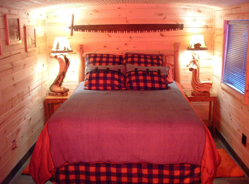 Cozy bedroom with a wooden bed, plaid bedding, and warm lighting, featuring rustic lamps and wooden walls.