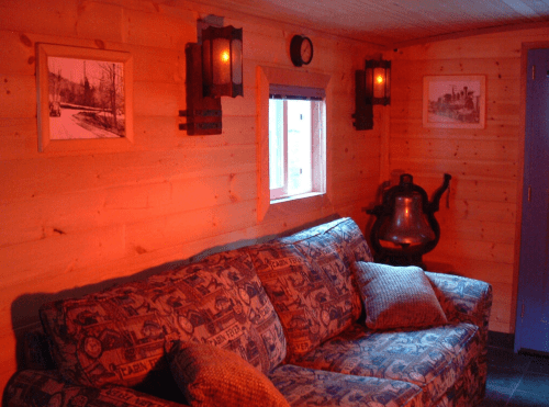 Cozy wooden cabin interior with a blue couch, warm lighting, and framed pictures on the walls.