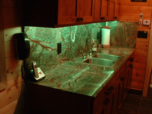A rustic kitchen with green under-cabinet lighting, a marble countertop, sink, and a vintage telephone.