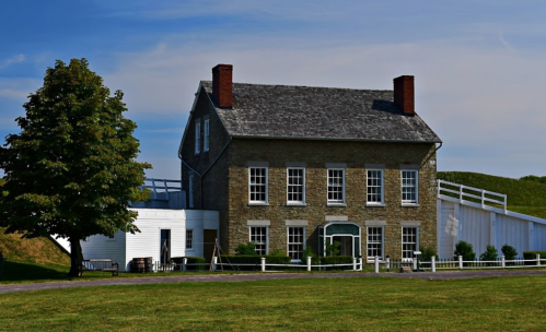 Historic stone building with large windows, surrounded by green grass and trees, under a clear blue sky.