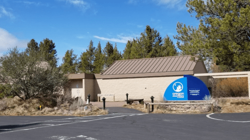 A building with a sign for Oregon State Parks, surrounded by trees and a clear blue sky.