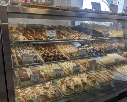 A display case filled with various pastries and desserts, including eclairs, cakes, and cream-filled treats.