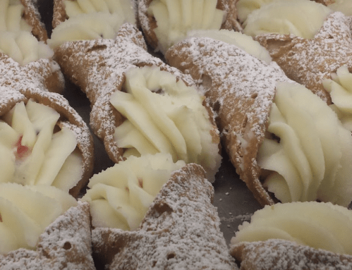 A close-up of freshly made cannoli filled with cream and dusted with powdered sugar.