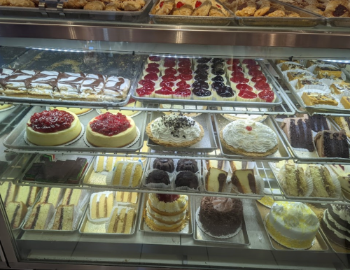 A display case filled with various cakes and pastries, including cheesecakes, layered cakes, and fruit-topped desserts.