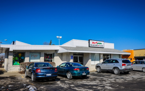 A bakery café with a sign, surrounded by parked cars under a clear blue sky.