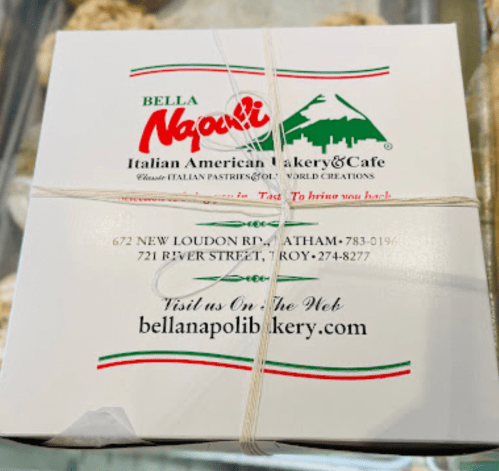 A white bakery box from Bella Napoli Italian American Bakery & Cafe, tied with string and featuring their logo and address.