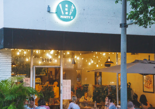 A cozy restaurant named "Minty Z" with outdoor seating, warm lights, and patrons enjoying their meals.